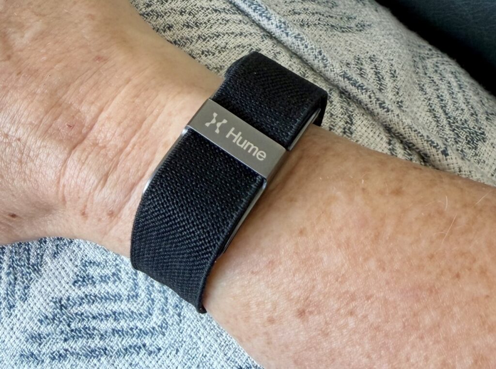A close-up of a Hume biometric wristband worn on a wrist, resting on a pillow, used to track HRV and recovery during a mid-day brain break for leaders practice.