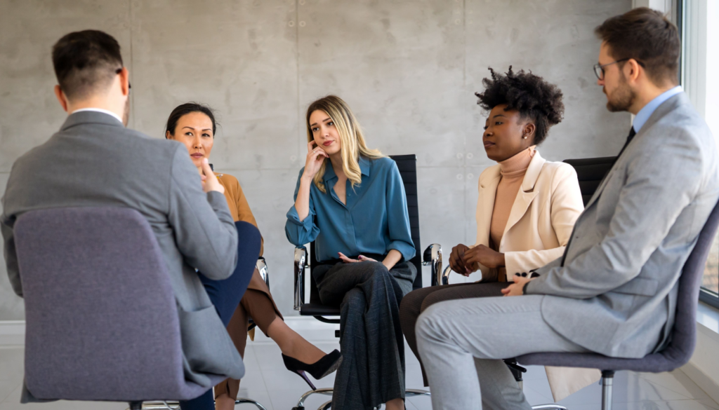 Team meeting where one employee is visibly disengaged while others speak, illustrating low psychological safety in the workplace.