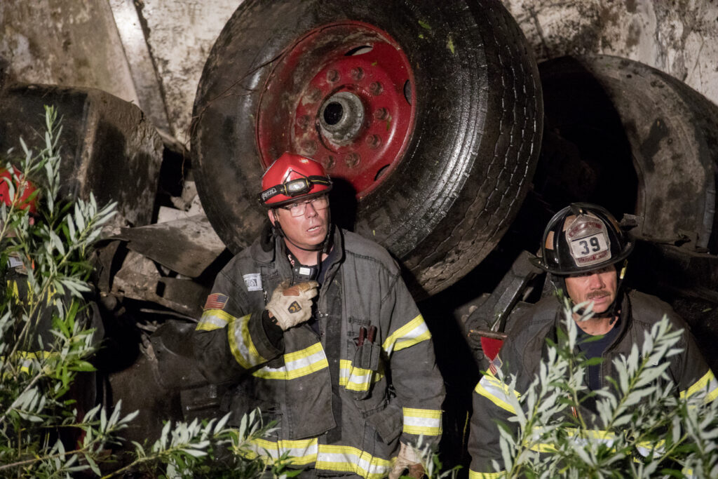 Scott Richardson, Division Chief and co-founder of EMPOWER2Evolve, commanding a cement truck rollover recovery operation in full turnout gear at night.