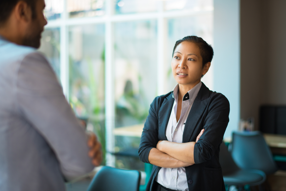 Woman with arms crossed looking defensively at colleague, illustrating why feedback feels like criticism