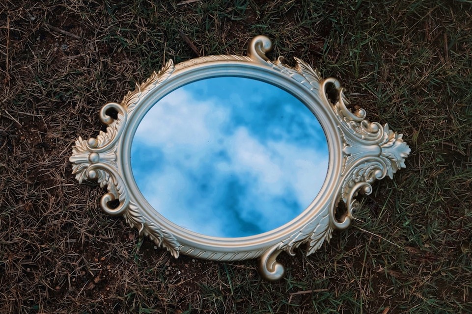 Ornate vintage mirror lying on grass reflecting a cloudy blue sky, symbolizing leadership self-awareness and reflection