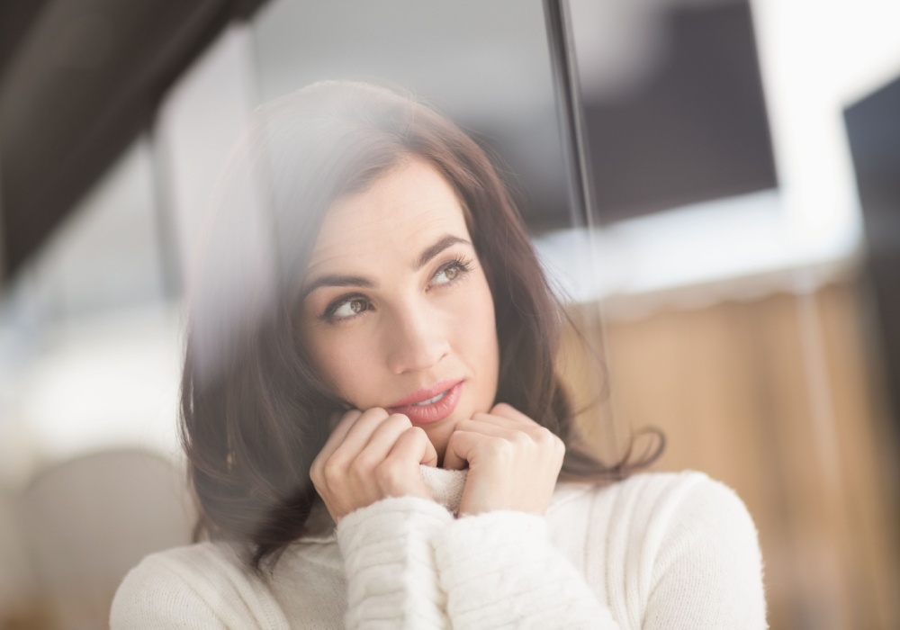 Woman resting her chin on her hands, gazing thoughtfully through a window, reflecting on leadership mindset